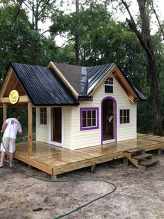 a man standing on a wooden platform in front of a small white house with purple trim