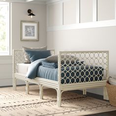 a white bed with blue sheets and pillows in a room next to a basket on the floor