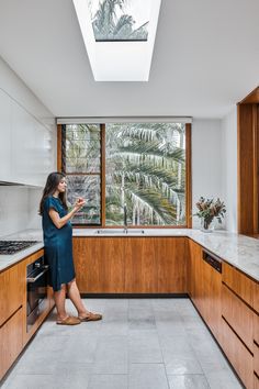 a woman standing in a kitchen looking at her cell phone with palm trees outside the window