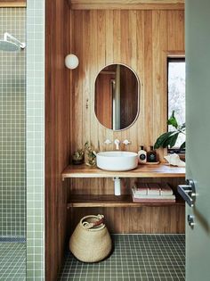 a bathroom with wood paneling and green tile on the floor, along with a round mirror