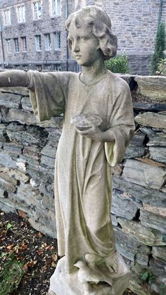 a statue of a woman holding a bird in her hand next to a stone wall