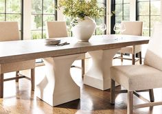 a dining room table with chairs and a vase filled with flowers on top of it