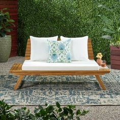 a wooden bench with pillows on it in front of a green wall and potted plants