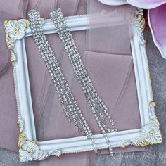 a white frame with some silver chains hanging from it's sides next to a pink flower