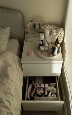 an open drawer in the corner of a bed with personal care items on it and a mirror