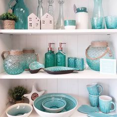 the shelves are filled with dishes, cups and vases in turquoise glassware on them