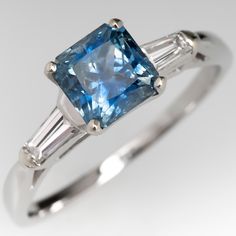 an engagement ring with a blue diamond and two baguets on the side, in white gold