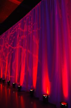 candles lit in front of a curtain with red light coming from the top and bottom