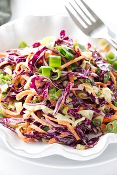 a white bowl filled with coleslaw slaw and carrots next to a fork