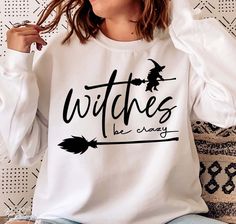 a woman sitting on a couch wearing a white witches be crazy shirt with black writing