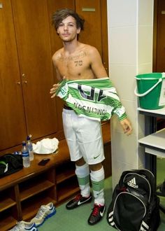 a shirtless man standing in a dressing room holding a green and white soccer jersey