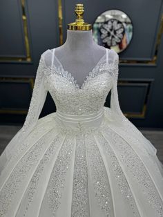 a white ball gown with long sleeves and beadings on the skirt is displayed in front of a clock