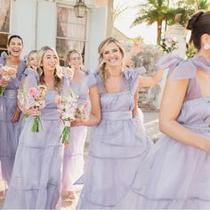 a group of bridesmaids in lavender colored dresses laughing and holding bouquets together