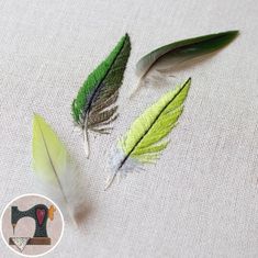 three green and white feathers sitting on top of a piece of cloth next to a sewing machine