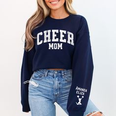 Elevate your cheer mom style with our cozy and customizable Cheer Mom Sweatshirt! Crafted for comfort and designed for the ultimate cheer supporter, this sweatshirt is a must-have for chilly game days and spirited practices. Key Features: Soft and warm fleece lining for maximum comfort. Stylish "Cheer Mom" design on the front to showcase your pride. Personalize the sleeve with your kids' names for a truly unique touch. Available in various sizes to ensure a perfect fit. Why Choose Our Cheer Mom Sweatshirt? Comfortable: Our sweatshirt is made for those cool evenings, providing warmth without sacrificing style. Customizable: Make it yours by adding your kids' names on the sleeve. Simply leave the names in the order notes during checkout. Versatile: Perfect for cheering on the sidelines, runn Crew Neck Tops For Cheerleading During Sports Season, Crew Neck Tops For Cheerleading Sports Season, School Spirit Tops For Cheerleading Sports Season, School Spirit Tops For Cheerleading During Sports Season, Custom Print Cotton Tops For Cheerleading, Varsity Crew Neck Tops For Cheerleading, Cotton Tops With Custom Print For Cheerleading, Cheerleading Team Spirit Crew Neck Tops, Team-colored Sweatshirt For Cheerleading With Team Name