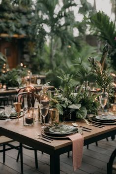 an outdoor table set with place settings and greenery in the background, surrounded by candles