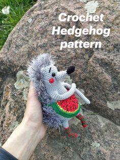 a hand is holding a crochet hedgehog toy in front of a rock