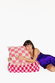 a woman in a blue dress is laying on a pink and white checkered pillow