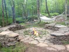 a stone fire pit in the middle of a wooded area with hammock hanging from trees