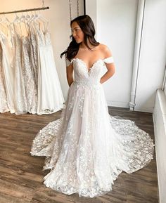 a woman standing in front of a rack of wedding dresses and looking at her dress