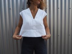 a woman standing in front of a metal wall wearing black pants and a white top