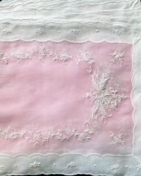 an embroidered pink and white pillow on a black surface with lace trim around the edges