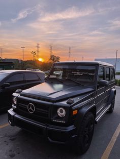 two cars parked in a parking lot with the sun setting over the ocean behind them