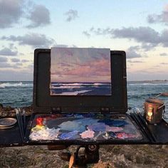 an artist's easel sitting on top of a rock next to the ocean