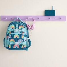 a blue backpack hanging on a purple wall with earbuds attached to it and a pair of pink headphones