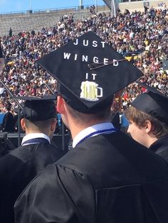 graduates in caps and gowns stand at the end of a graduation ceremony as an audience looks on