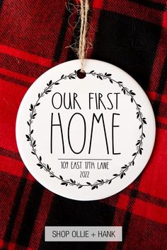 a white ornament hanging from a red and black checkered blanket with the words our first home on it