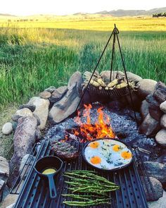 an open fire pit with food on it and asparagus in the foreground