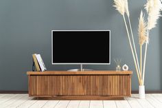 a flat screen tv sitting on top of a wooden cabinet next to a vase with dry grass