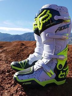 a pair of white and green shoes sitting on top of a dirt covered ground with mountains in the background