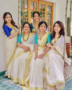 four women in white and yellow sari sitting on a swing