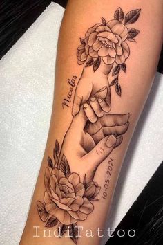 a woman's arm with roses and two hands holding each other on her forearm