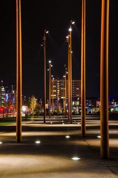 the lights are shining brightly in the night sky over an empty parking lot with tall poles and street lamps