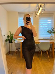 a woman in a black dress taking a selfie with her cell phone while standing in front of a dining room table