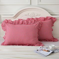 two red and white gingham pillows sitting on top of a bed next to a magazine