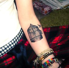 a woman's arm with a bird in a cage tattoo on her left wrist