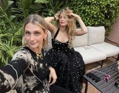 two women are posing for the camera in front of a couch and table with flowers on it