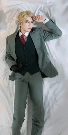 a young man in a suit and tie laying on a white sheet with his hands behind his head