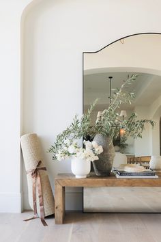 a vase with flowers on a wooden table in front of a mirror and lamp fixture