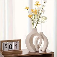 two vases with flowers in them sitting on a table next to a calendar and clock