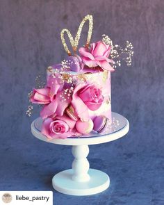 a cake with pink roses and pearls on top is sitting on a stand against a blue background