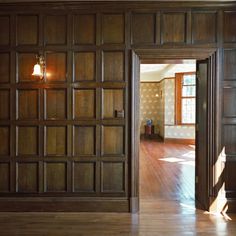 an empty room with wood paneling on the walls and wooden floors, as well as a door leading to another room