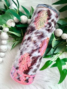 a pink and black patterned tumbler sitting next to some green leaves on top of a white fur covered floor