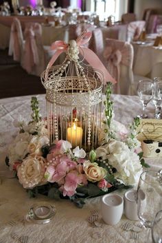 a birdcage filled with flowers and candles on top of a white table cloth