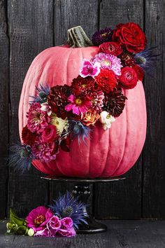 a pink pumpkin decorated with flowers on top of a black cake stand next to a wooden wall