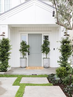 a white house with two potted plants on the front door and side walk way